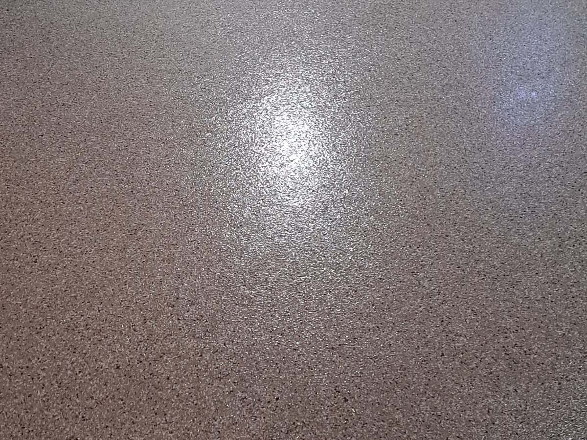 Flake floor under overhead shop light — the polyaspartic seal picks up every bit of brightness and wipes clean of chemicals.
