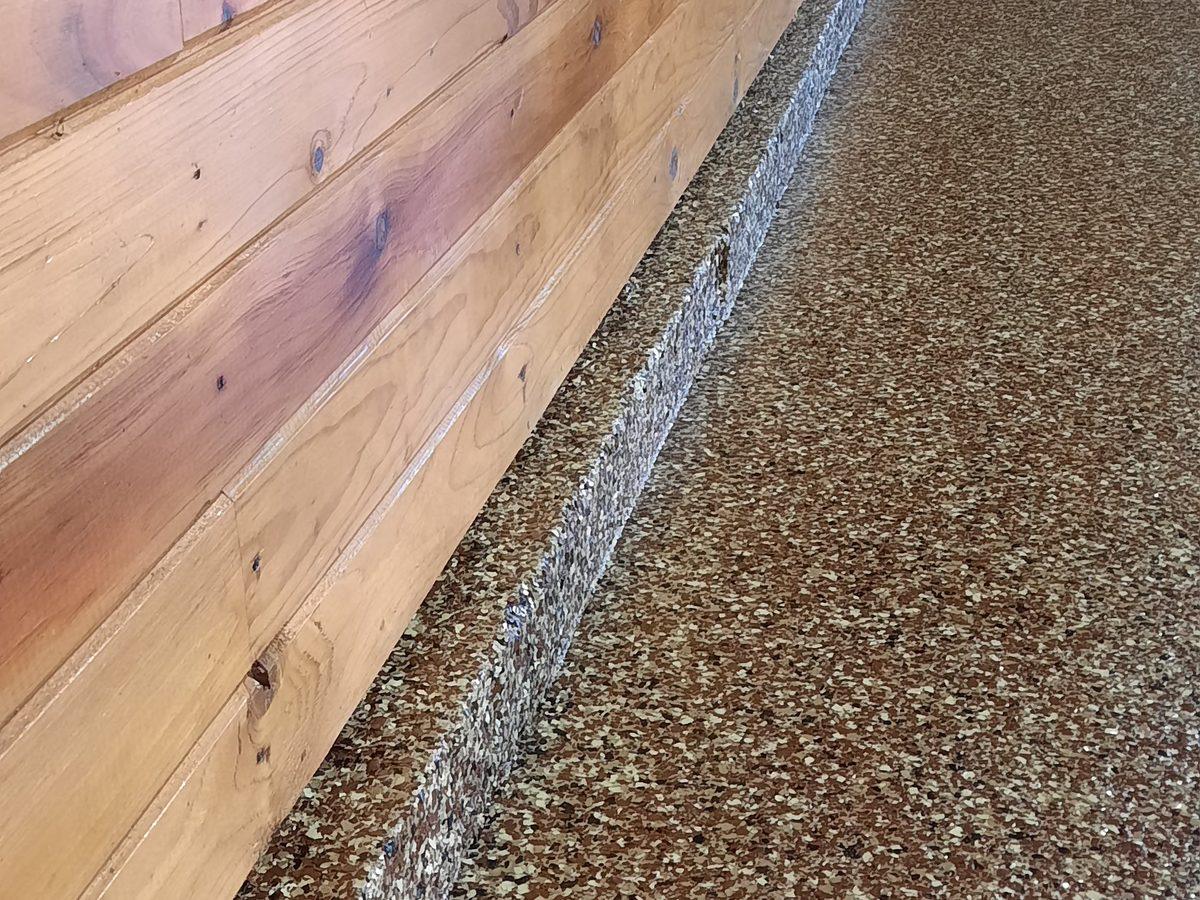 Brown flake floor meeting a tongue-and-groove wood wall — the edge rolls clean, no caulk line, no gap.